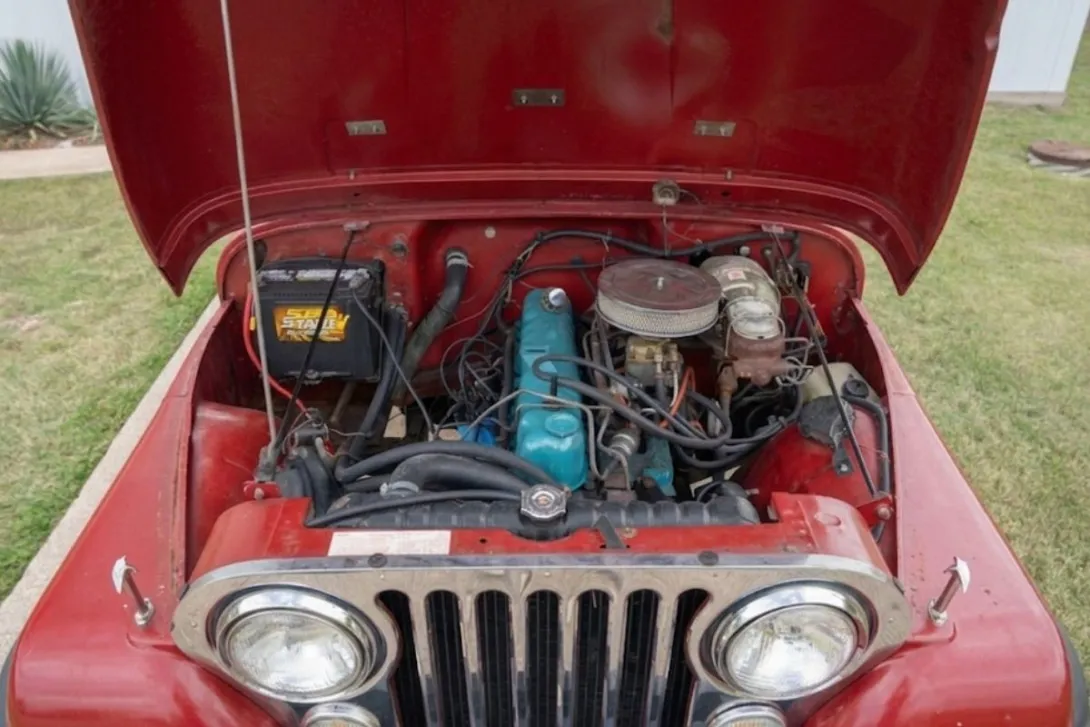 Red Jeep CJ with hood up showing AMC inline-six engine bay, radiator, and cooling system components